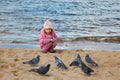 Little girl sits on beach at water edge in autumn Royalty Free Stock Photo