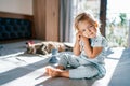 Little girl sits on a bed hugging a teddy bear next to a sleeping tabby cat Royalty Free Stock Photo