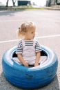 Little girl sits in a big blue tire on the playground and looks away Royalty Free Stock Photo