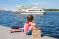 A little girl sits on the city promenade on a sunny day. The view from the back. Life style