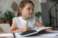 Little girl sits at the desl at home and does homework, self study of the material, reading book