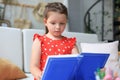 Little girl sits at the desl at home and does homework, self study of the material, reading book