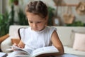 Little girl sits at the desl at home and does homework, self study of the material, reading book