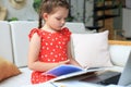 Little girl sits at the desl at home and does homework, self study of the material, reading book