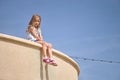 little girl sits on the edge of the wall dangling legs, stone wall her legs dangling in the air Royalty Free Stock Photo