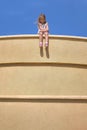 little girl sits on the edge of the wall dangling legs, stone wall her legs dangling in the air Royalty Free Stock Photo