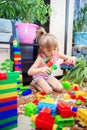 A little girl sits on the floor at home and plays a multi-colored plastic constructor. A child playing a toy train Royalty Free Stock Photo