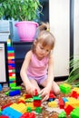 A little girl sits on the floor at home and plays a multi-colored plastic constructor. A child playing a toy train Royalty Free Stock Photo