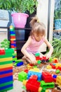 A little girl sits on the floor at home and plays a multi-colored plastic constructor. A child playing a toy train Royalty Free Stock Photo