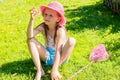 A little girl in a pink hat sits on the fresh grass and holds in her hands a butterfly caught in a butterfly net. Royalty Free Stock Photo