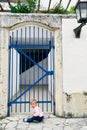 Little girl sits in front of a metal lattice gate near the house