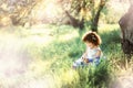 Little girl sits in grass in garden with flovers. Springtime. Sunset. Dangerous harvest bug possible. Allergy season. Natural