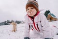 Little girl sits on her knees on a snowy hill and tries the snow with a grimace Royalty Free Stock Photo