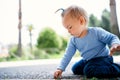 Little girl sits on her lap and picks the asphalt in a green park. Side view Royalty Free Stock Photo