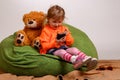 Little girl sits on a high green pillow and plays with mobile ph Royalty Free Stock Photo