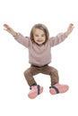 A little girl sits and laughs with her hands up. Cute child in brown jeans and a pink sweater. Happiness, positivity and joy.