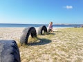 A little girl sits near the sea on a tire buried in the ground until half