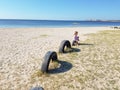 A little girl sits near the sea on a tire buried in the ground until half