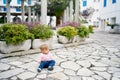 Little girl sits on paving slabs near flowerpots with green bushes on the background of buildings Royalty Free Stock Photo