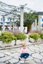 Little girl sits on paving slabs near flowerpots with green bushes Royalty Free Stock Photo