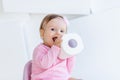 A little girl sits on a potty in pink clothes in a bright room and plays with toilet paper Royalty Free Stock Photo