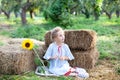 Little girl sits on roll of haystacks in garden. child sits in straw and enjoying nature on a fall day in countryside. Sunflower.