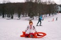 Little girl sits on a sled on a snowy plain against the backdrop of sledgers and skiers