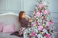 Little girl sits on a sofa and touches a tree toys on in Christmas tree at home