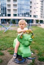 Little girl sits on a spring swing on a playground in the courtyard of an apartment building Royalty Free Stock Photo