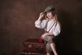 Little girl sits on suitcases. vintage style photography. child in a white shirt, pants and a hat with a visor. studio. brown