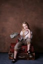 Little girl sits on suitcases. vintage style photography. child in a white shirt, pants and a hat with a visor. studio. brown