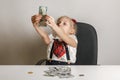 A little girl sits at a table in front of a stack of hundred-dollar bills and examines one of them for light, checks for falsity Royalty Free Stock Photo