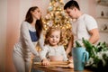 Little girl sits at the table and her parents stand in the background