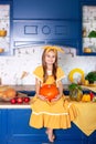 Little girl sits on table in kitchen holds big pumpkin. Harvesting. Healthy nutrition, vegetarianism, vitamins, vegetables. Cute c