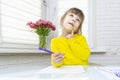 Little girl sits at a table in a white room and draws Royalty Free Stock Photo