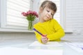 little girl sits at a table in a white room and draws Royalty Free Stock Photo