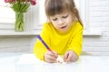 little girl sits at a table in a white room and draws Royalty Free Stock Photo