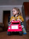 Little girl sits in a toy car and makes funny face