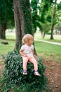 Little girl sits on a tree stump entwined with green ivy in the park Royalty Free Stock Photo