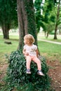 Little girl sits on a tree stump entwined with green ivy in the park, turning her head Royalty Free Stock Photo