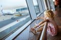 little girl sits by window at airport and points finger at plane. child in airport departure lounge. Girl sitting on Royalty Free Stock Photo