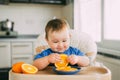 Little girl sitting in baby chair, eating an orange Royalty Free Stock Photo