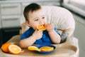 Little girl sitting in baby chair, eating an orange Royalty Free Stock Photo