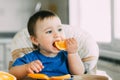 Little girl sitting in baby chair, eating an orange Royalty Free Stock Photo