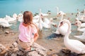 Little girl sitting on the beach with swans Royalty Free Stock Photo