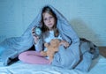 Little girl sitting on bed with teddy bear and alarm clock sleepless at night feeling restless