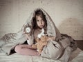 Little girl sitting on bed with teddy bear and alarm clock sleepless at night suffering insomnia