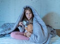 Little girl sitting on bed with teddy bear and alarm clock sleepless at night suffering insomnia