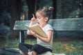 Little girl is sitting on a bench and is reading a book Royalty Free Stock Photo