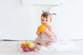 A little girl is sitting in a bright room with a plate of fruit and eating an orange Royalty Free Stock Photo